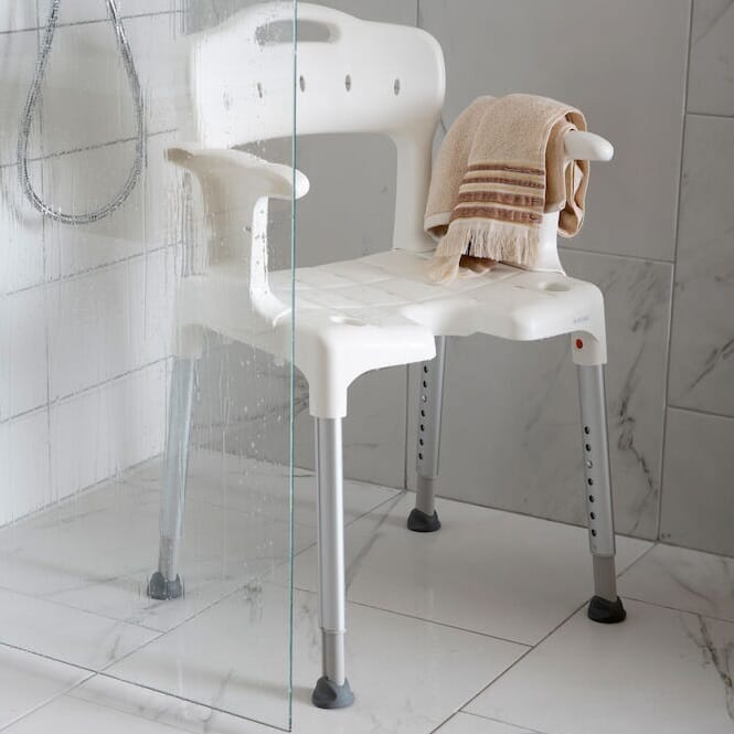 Angled view of Etac Swift Shower Chair with Arm Supports with moulded seat, supportive backrest and height-adjustable legs on a plain background.