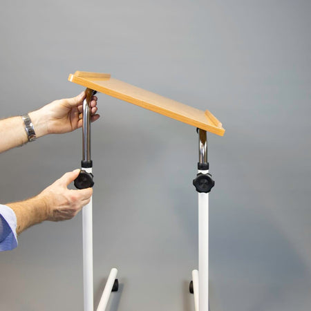 Close-up of hands adjusting the height or tilt of NRS Beech Overbed Overchair Table, showing the easy-turn knobs.