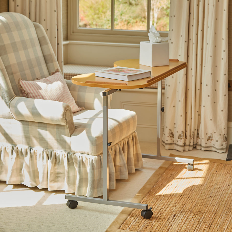 Angled view of NRS Curved Adjustable Overbed Table with beech-effect tilting table top and white U-shaped base on castors against a neutral background.