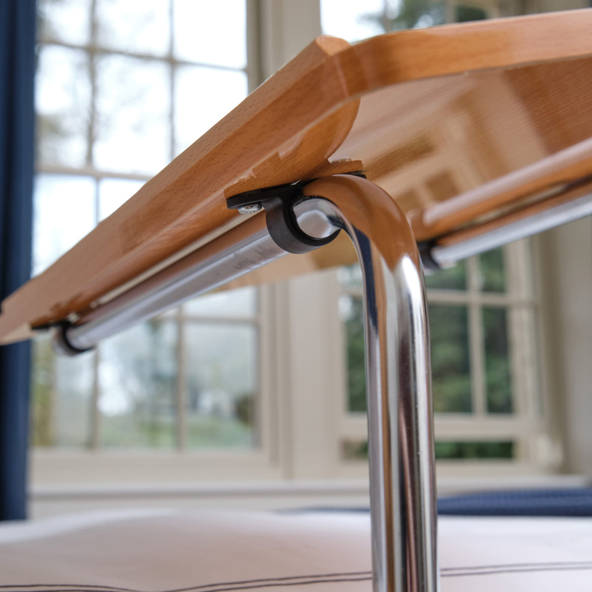 Side view of NRS Divan Overbed Table showing the tilting top and height-adjustable chrome stems.