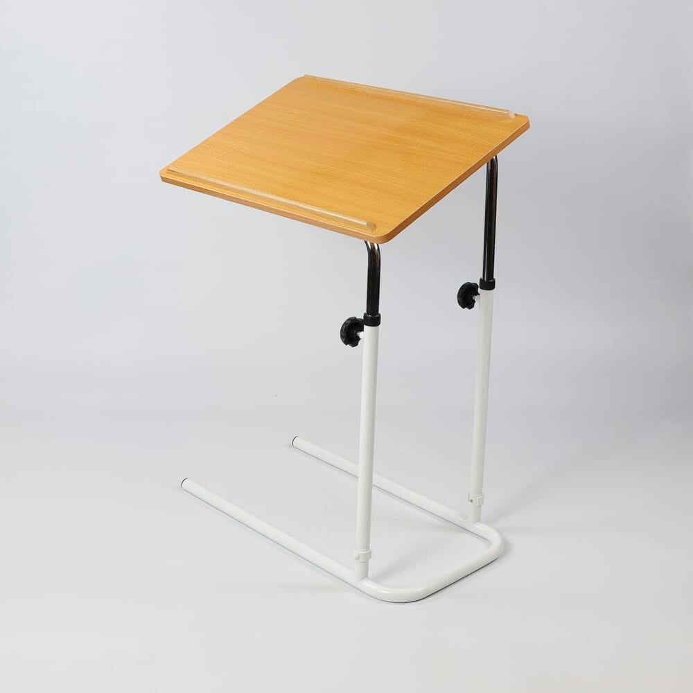 Front view of NRS Divan Overbed Table with the table top tilted, showing the raised lips and attractive beech finish.