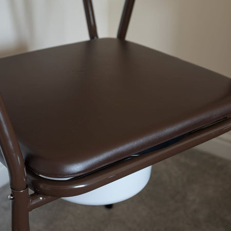 Person emptying or cleaning the commode pan of NRS Dovedale Adjustable Commode with Detachable Arms into a standard toilet.