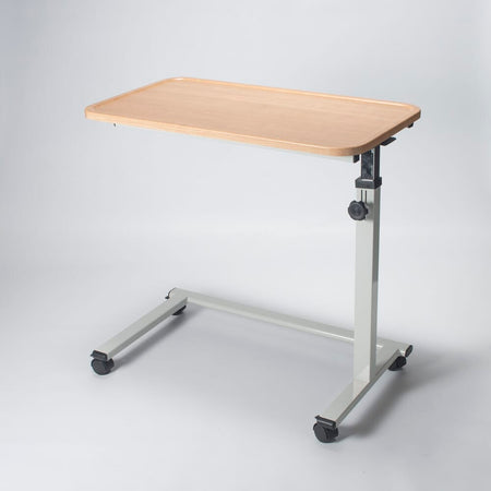 Angled view of NRS Easylift Home Height Adjustable Overchair Table with beech-effect tilting table top and white U-shaped base on castors against a neutral background.