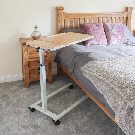 Side view of NRS Easylift Home Tilting Overbed Table showing the tilting top and height-adjustable chrome stems.