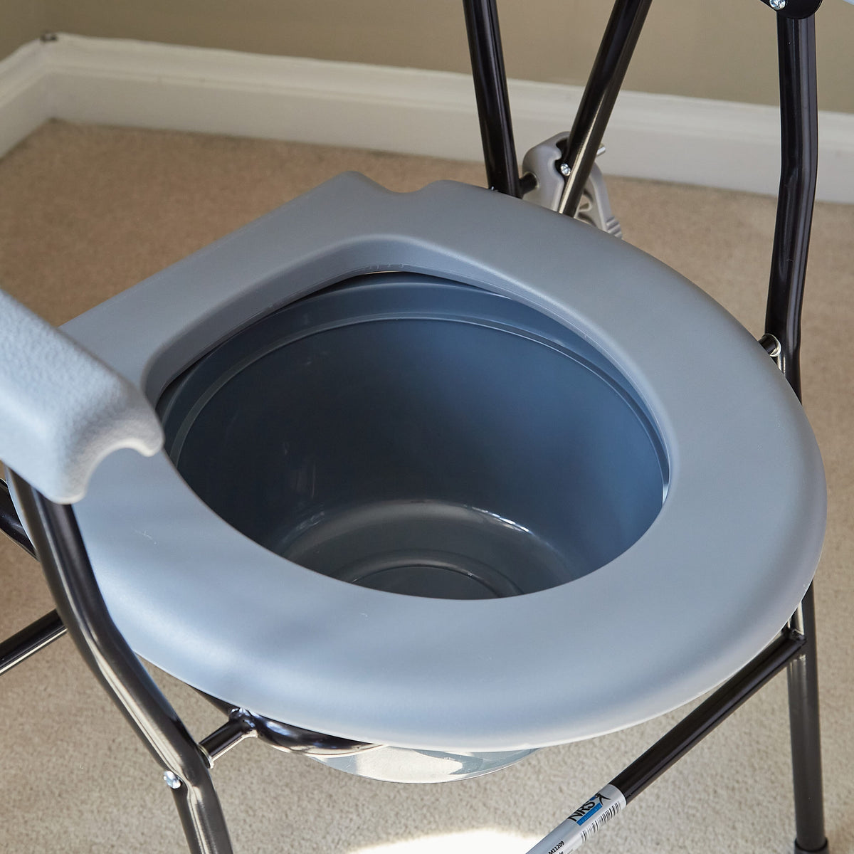 NRS Folding Commode positioned in a home environment such as a bedroom or bathroom, demonstrating its discreet appearance.