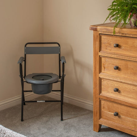 NRS Folding Commode in use in a home setting, with lid open to illustrate accessibility and convenience.
