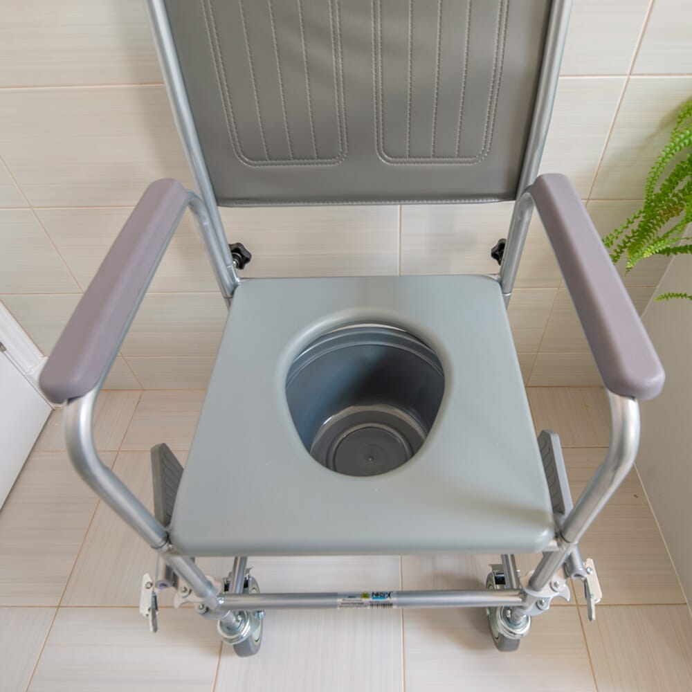 NRS Wheeled Commode in use in a home setting, with lid open to illustrate accessibility and convenience.