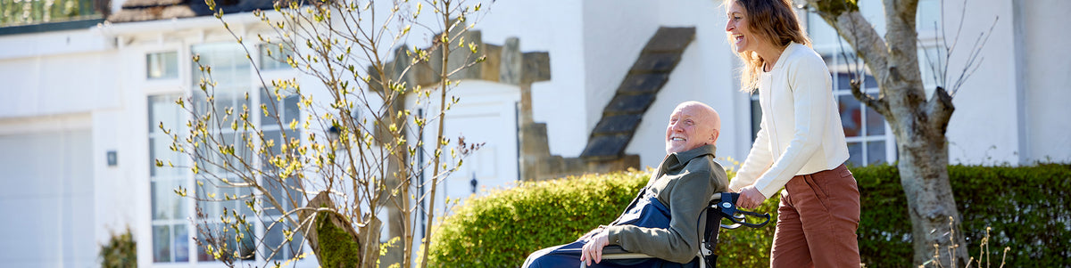 Woman pushing a man in a wheelchair in a garden setting.